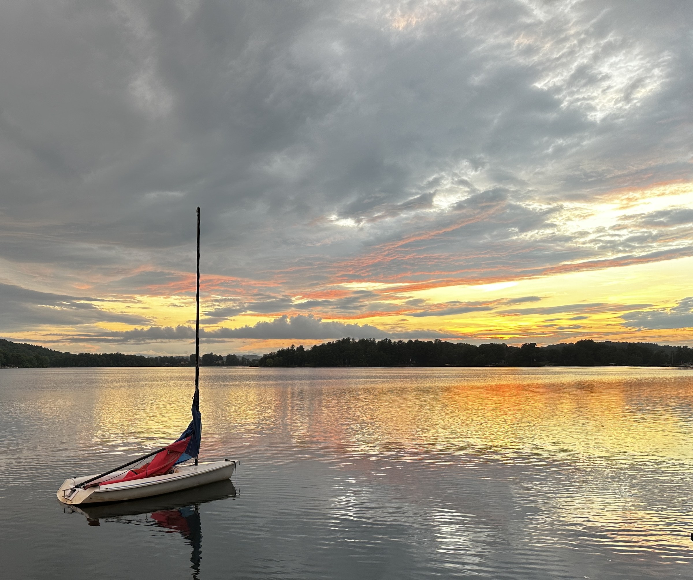 A small sailboat at rest on Copake Lake beneath a luminous evening sky