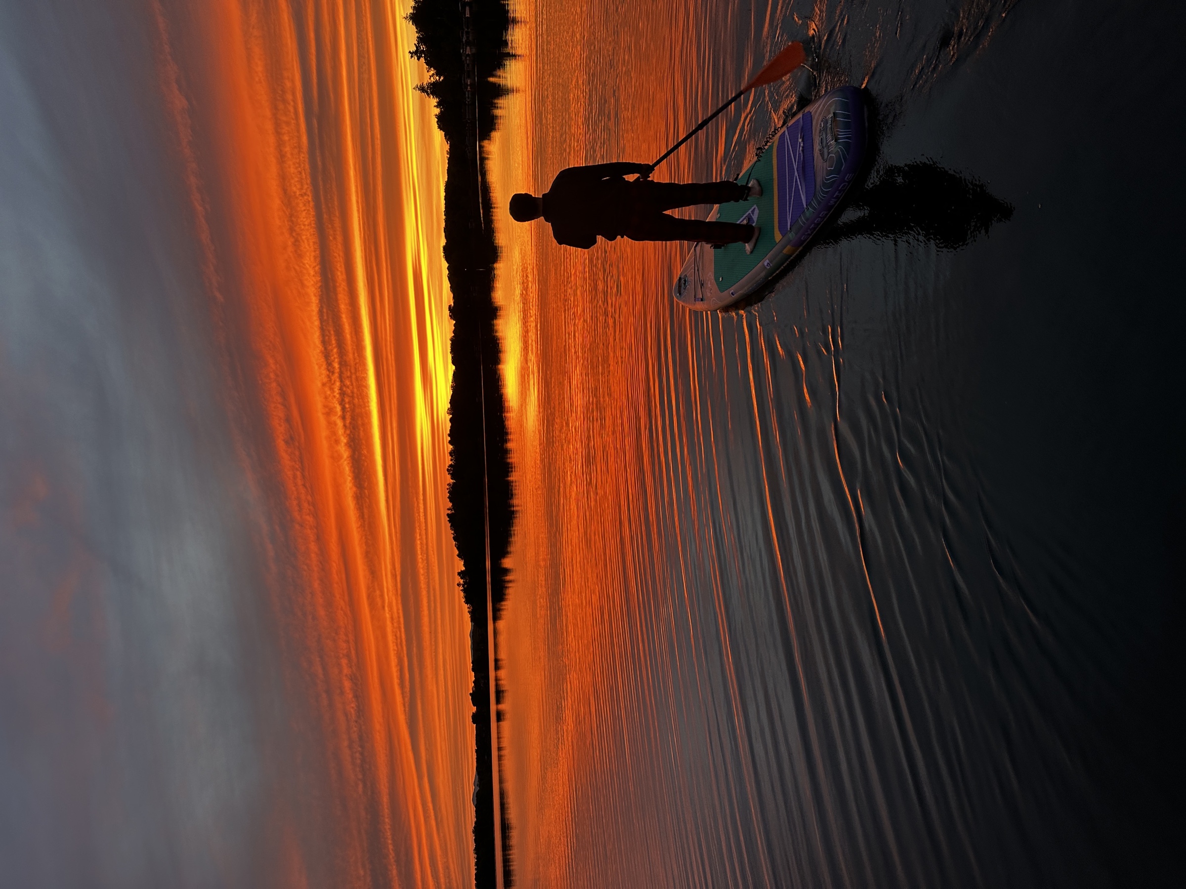 A paddleboarder crossing Copake Lake beneath a vivid orange sunset